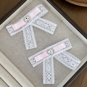 Detailed macro of white lace hair clips with pink ribbons and heart-shaped rhinestones