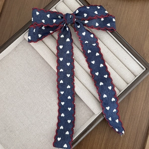 Close-up of denim-style heart print bow hair clip with red scalloped edge on display tray