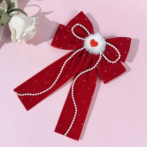 Close-up of red velvet bow hair clip with pearl chains and heart center on pink background