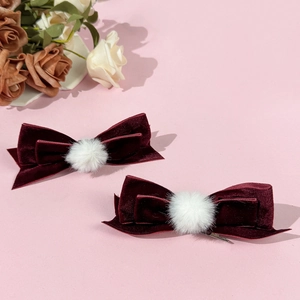 Detalle de dos lazos para el pelo de terciopelo granate con pompones blancos y clips de metal