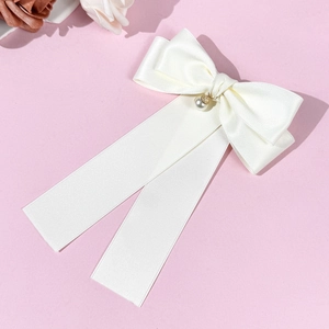 Dettaglio dell'elegante fiocco per capelli in raso bianco con perla su uno sfondo rosa