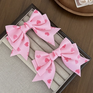 Détail de barrettes nœuds roses avec motifs de cœurs rouges sur un plateau à bijoux