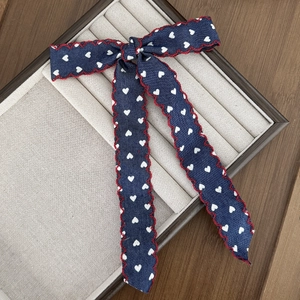 Close-up of denim blue bow hair clip with white heart prints and red scalloped edges