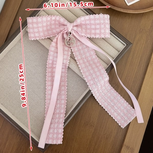 Detailed view of pink plaid bow hair clip with silver LOVE charm on beige velvet tray