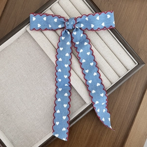 Detailed view of denim style bow hair clip with white heart prints and red wavy stitching
