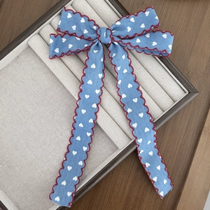 Detailed close-up of blue heart denim hair clip with elegant red wavy stitched edges