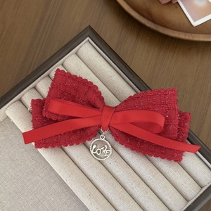 Close-up of red tweed bow hair clip with silk ribbons and silver LOVE metal pendant
