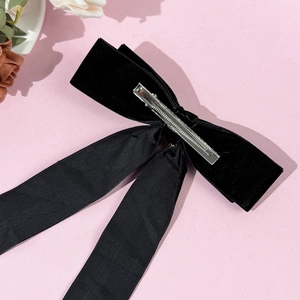 Eleganter schwarzer Samtbogen-Haarclip mit langen Bändern und Perlen auf rosa Hintergrund