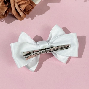 Pince à cheveux nœud en satin blanc élégante avec clip en métal sur fond rose doux