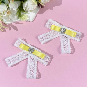 Close-up of white lace bow clips with yellow ribbon and sparkling heart rhinestone