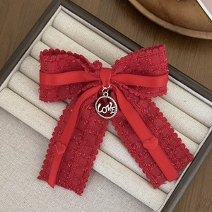 Macro detail of red tweed bow hair clip with silver LOVE charm on jewelry tray