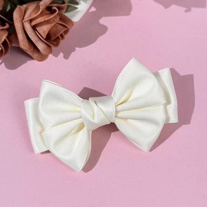 Barrette à cheveux élégante avec nœud en satin blanc crème sur un fond rose poudré