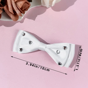 Detailed view of white satin bow hair clip with silver hearts on a pink background