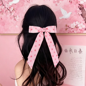 Pink heart pattern bow hair clip with long ribbons worn on wavy black hair