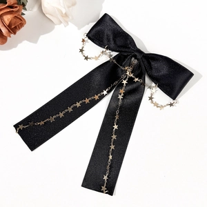 Détail d'un nœud papillon en satin noir avec chaîne pendante à étoiles dorées sur fond blanc