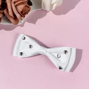 Detail of a white satin bow hair clip with sparkling silver heart rhinestones on pink background