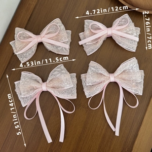 Pink lace bow hair clips set with ribbon tassels on a dark wood background