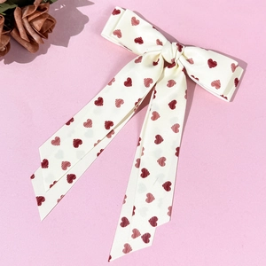 Cream satin hair bow clip with red heart prints and long ribbons on pink background