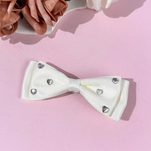 Detail of white satin bow hair clip decorated with sparkling heart-shaped rhinestones