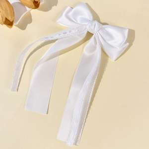Detail of white satin bow hair clip featuring delicate lace edges and long flowing ribbons