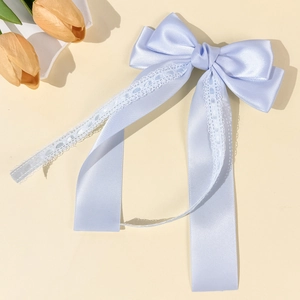 Detailed close-up of light blue satin bow hair clip with white floral lace trim and long ribbons