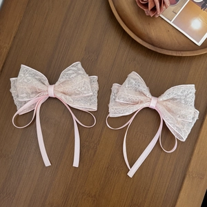 A pair of sweet pink lace bow hair clips with long ribbons on a wooden background