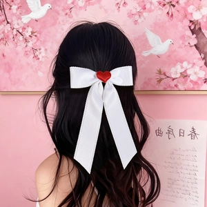 Detailed view of white satin bow hair clip with red heart and long ribbons on model hair
