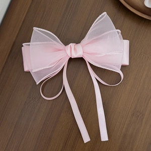 Pink layered mesh bow hair clip with long ribbons on a dark wooden background