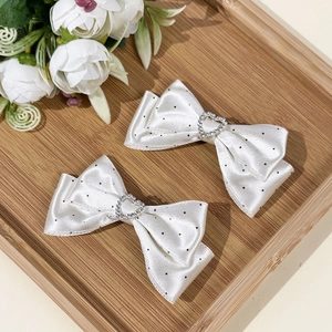 Detalle de pinzas para el pelo con lazos de satén blanco, lunares negros y corazón de strass