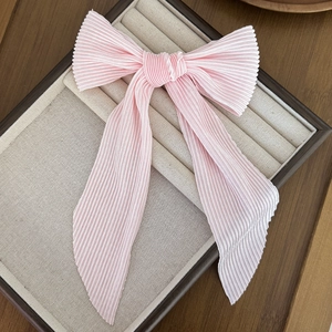 Detail of light pink plissé pleated bow hair clip with long ribbons on a velvet stand