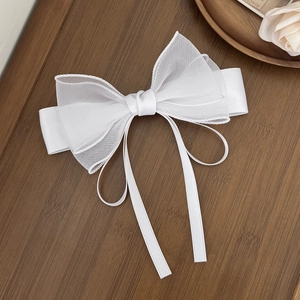 Close-up of white mesh bow hair clip with elegant long ribbons on dark wood background