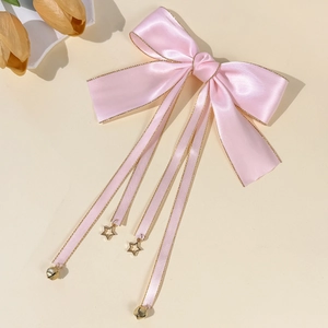 Dettaglio fiocco per capelli in raso rosa con bordo dorato e ciondoli a stella
