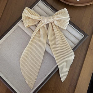 Macro detail of elegant champagne pleated chiffon bow hair clip in a luxury jewelry box
