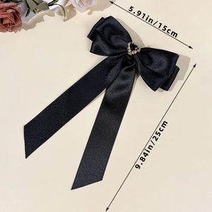 Detail of black satin bow hair clip with rhinestone heart and long ribbon streamers