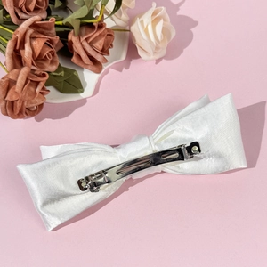 Elegant white satin bow hair clip with a silver metal spring clip on a pink backdrop