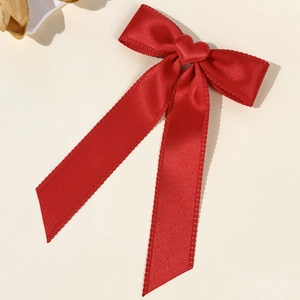 Elegant red silk bow hair clip with a centered heart accent on a minimalist background