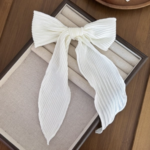 Detail of white pleated bow hair clip with long flowing ribbons on a jewelry display tray