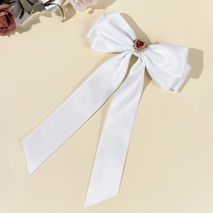 Close-up of a white satin bow hair clip with a red heart rhinestone and long ribbons