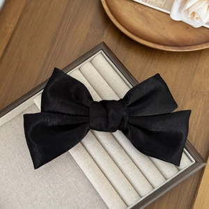 Détail d'une pince à cheveux avec nœud en satin noir sur un plateau à bijoux chic