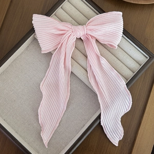 Detailed view of pink pleated silk bow hair clip on a warm beige jewelry display