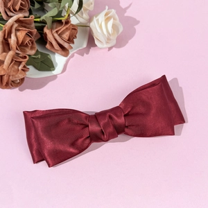 Elegant dark red satin bow hair clip with a smooth glossy texture on pink background