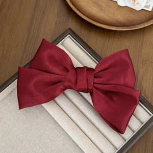 Détail d'une pince à cheveux élégante en satin bordeaux sur un plateau en lin beige