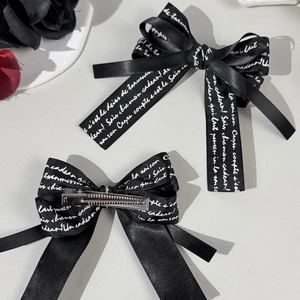 Pair of black satin bow hair clips with white script lettering and metal duckbill clip