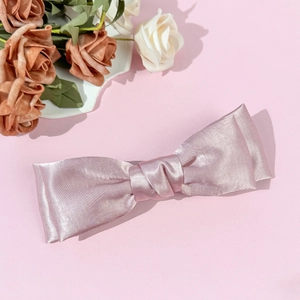 Detail of elegant pale pink satin bow hair clip with smooth silk texture and floral accent