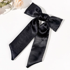 Detail of elegant black satin hair bow with long ribbons on a minimalist white background