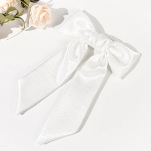 Detail of elegant white satin bow hair clip with long flowing ribbons and silky texture