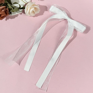 Detail of white tulle bow hair clip with elegant ribbons on soft pink background
