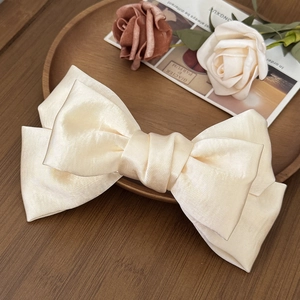 Detailed view of oversized cream satin bow hair clip on a wooden tray with roses