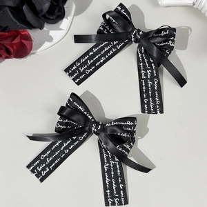 Detailed macro view of two black satin ribbon bow clips with artistic white French text print