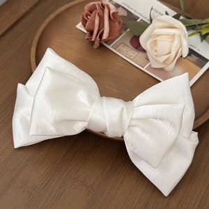Detailed 45-degree macro view of pearl white satin bow hair clip with silk texture